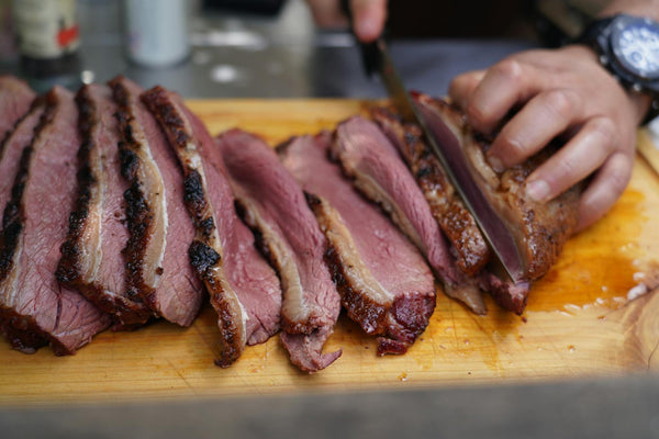 Close-up of a hand slicing juicy, smoked beef brisket on a wooden cutting board, showcasing deliciously cooked meat.