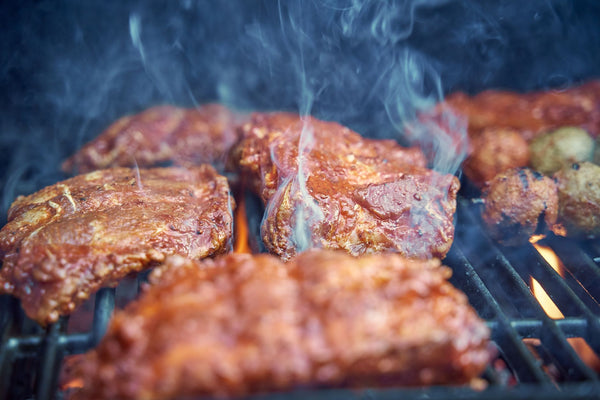 Sizzling marinated meat cooking on a barbecue grill with smoky steam rising.