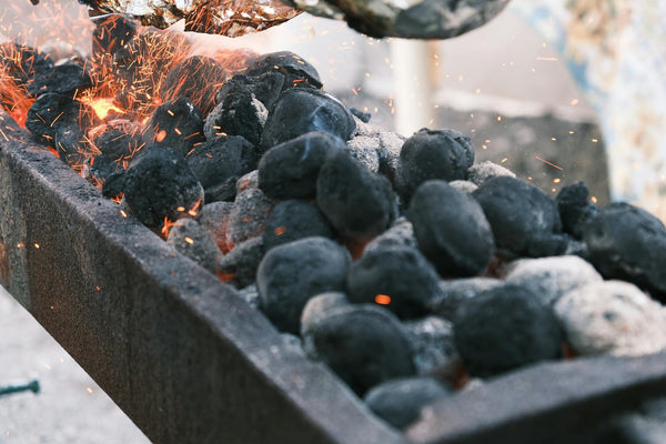 Sparks fly from burning charcoal on a barbecue grill, creating a hot and fiery atmosphere.