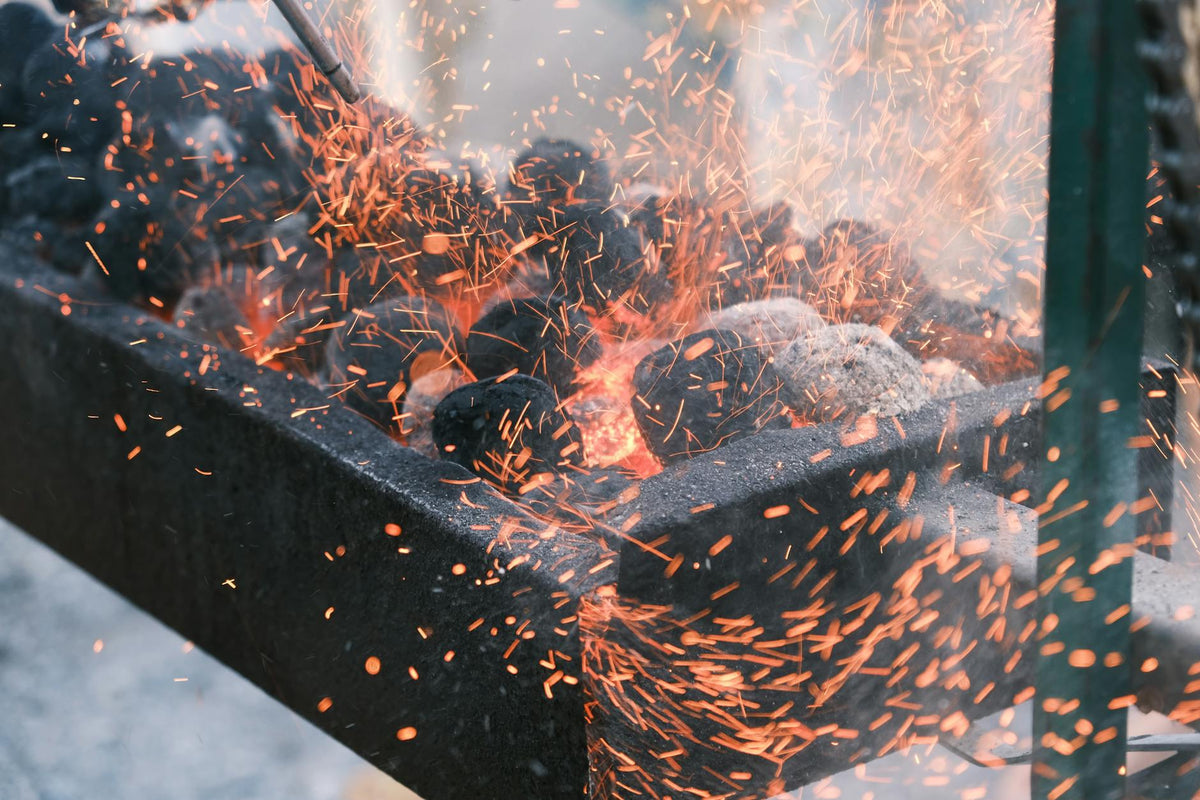 Close-up view of hot charcoal igniting with bright sparks flying upwards, showcasing intense heat energy.