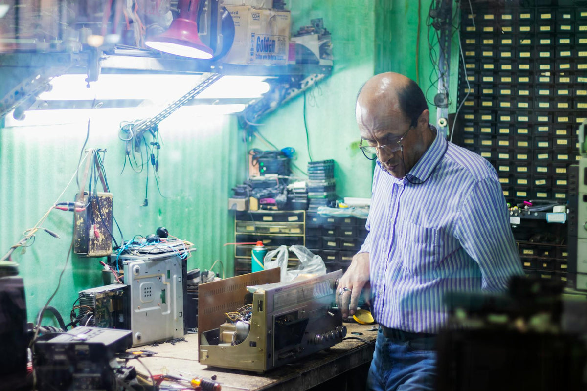 Man focusing on repairing electronic equipment in cluttered workshop with various tools.