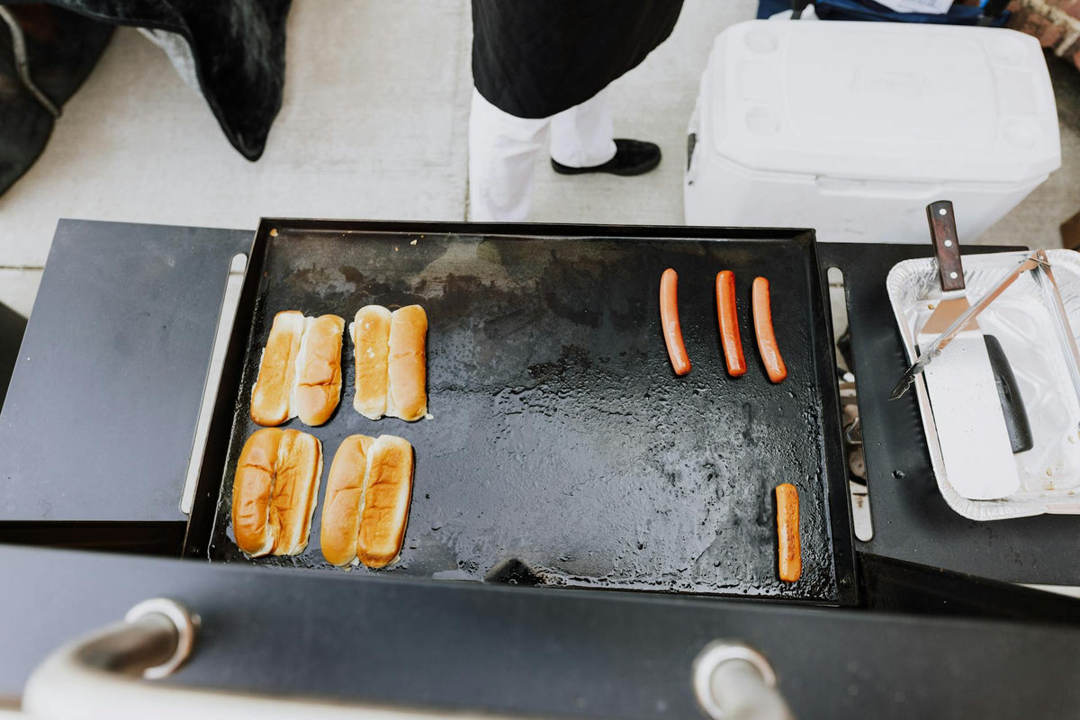 Overhead view of hot dogs and buns grilling at an outdoor BBQ setting.