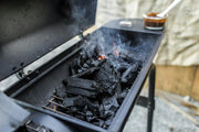 Close-up of a charcoal grill emitting smoke, showcasing burning coals and outdoor cooking setup.