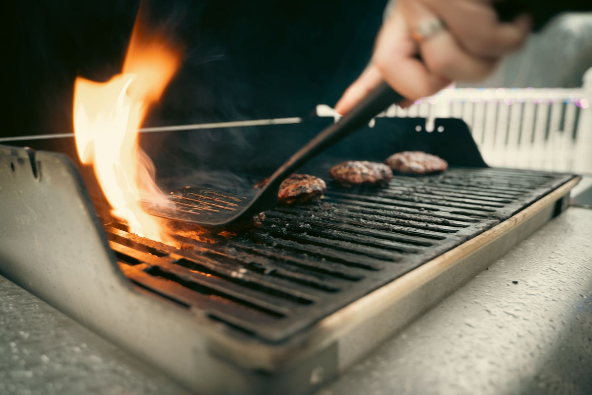 Close-up view of juicy burgers sizzling on a flaming outdoor grill.