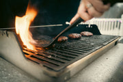 Close-up view of juicy burgers sizzling on a flaming outdoor grill.