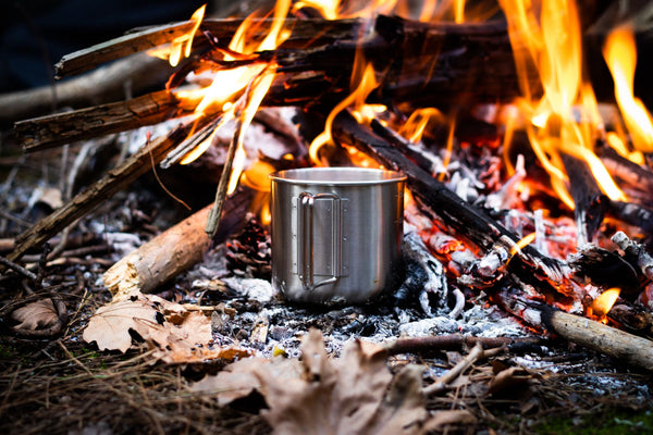 A campfire with flames and a stainless steel mug, perfect for outdoor adventures.
