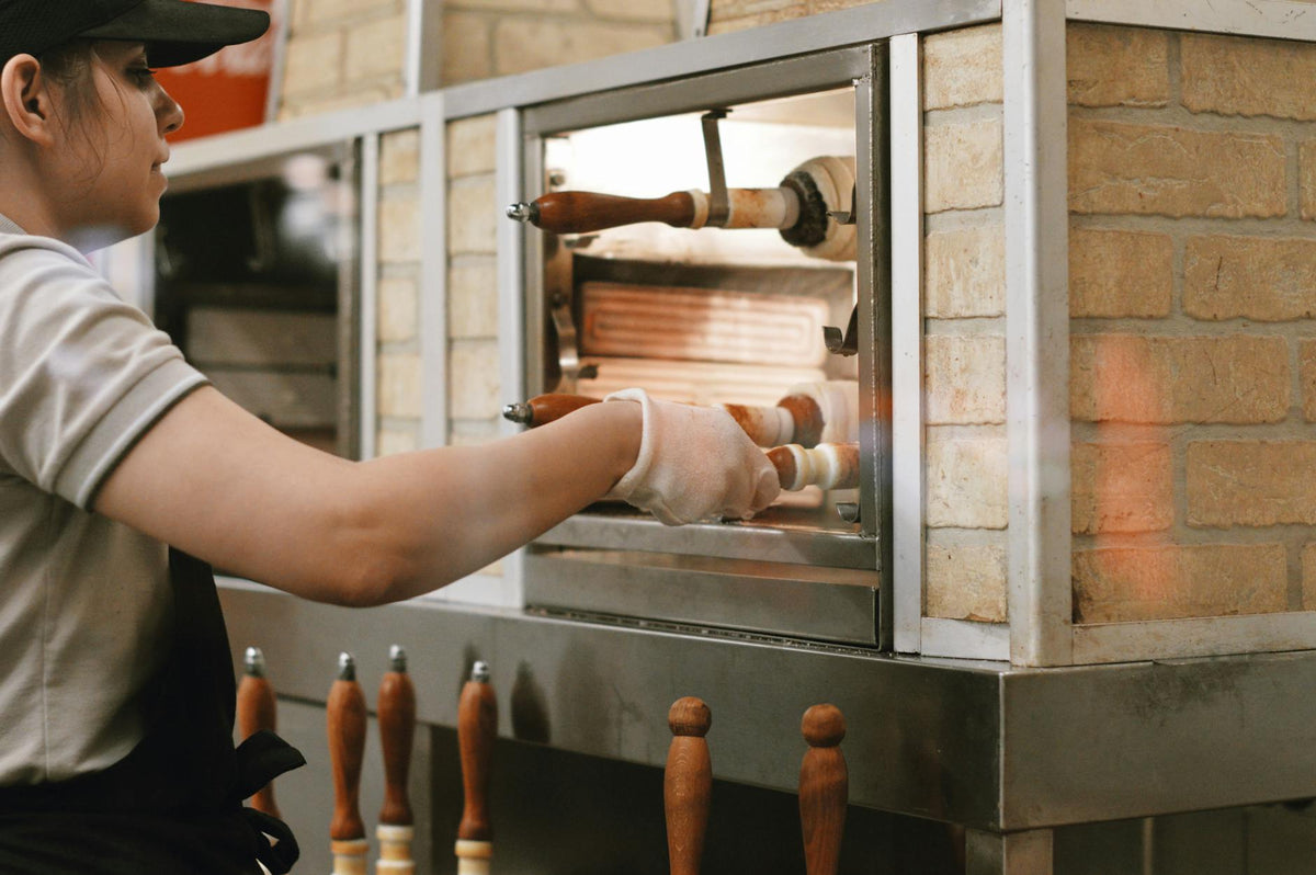 A female worker operates a traditional brick pizza oven in a pizzeria setting.