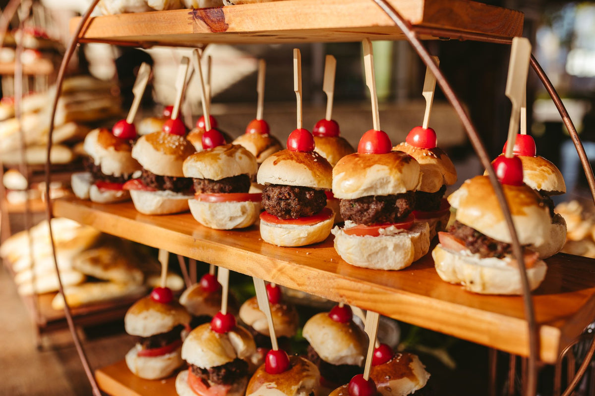 Close-up of freshly made mini burgers with tomatoes at an outdoor event setup.