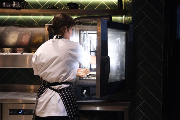 A chef in a striped apron prepares food using a commercial kitchen oven.