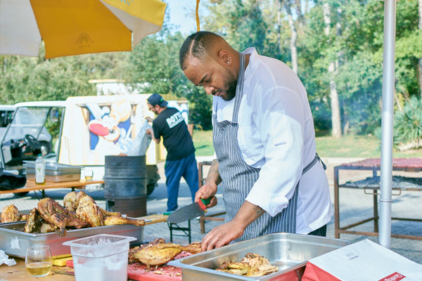 Chef skillfully carving grilled chicken at an outdoor culinary event.