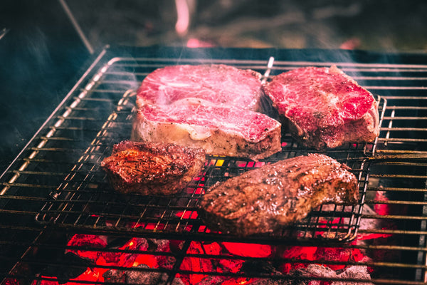 Juicy steaks sizzling on a barbecue grill over red-hot coals, perfect for outdoor cooking.