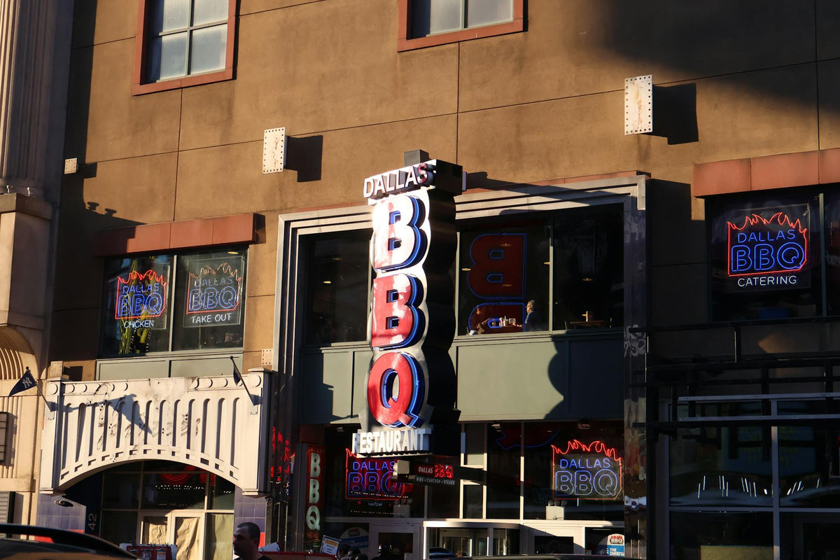 Neon signage of Dallas BBQ Restaurant illuminated in an urban environment at sunset.