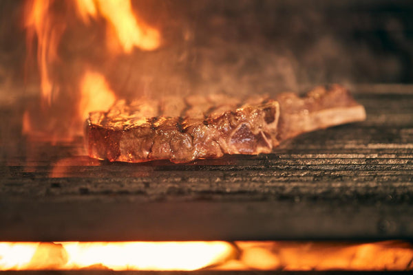 Juicy ribeye steak cooking over an open fire grill with flames, showcasing delicious grilling action.