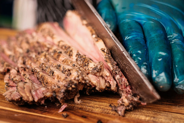 Barbecue brisket being expertly sliced by a gloved hand on a wooden cutting board.