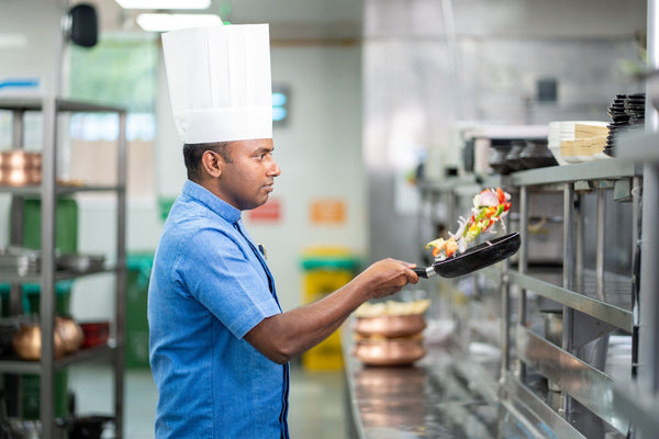 Professional chef tossing a pan of vegetables in a commercial kitchen, showcasing culinary skills.