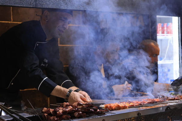Chef expertly grills skewers in a smoky kitchen, showcasing culinary skills and vibrant ingredients.