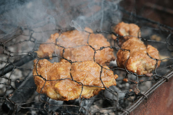 Close-up of traditional Indonesian grilled chicken sizzling on a barbecue grill.