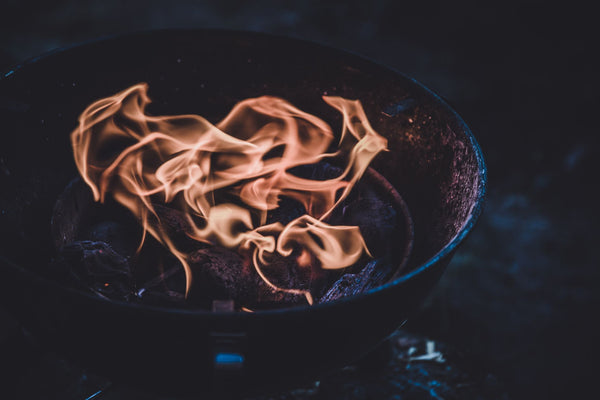 Close-up of orange flames flickering over charcoal in a grill, creating a warm glow against a dark background.