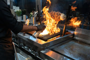 Chef grilling meat with spectacular flames in a modern kitchen setup.