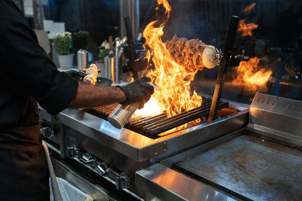Chef grilling meat with spectacular flames in a modern kitchen setup.