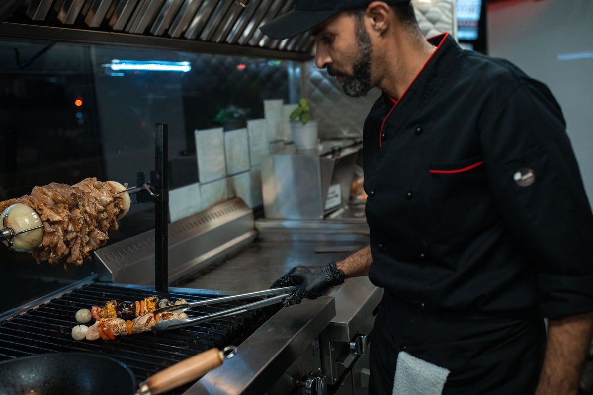 Chef grilling skewers with precision in a professional kitchen setting.