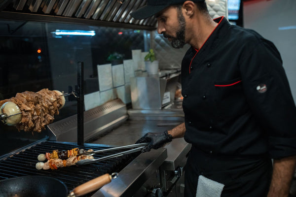 Chef grilling skewers with precision in a professional kitchen setting.