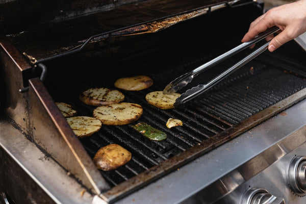 Unrecognizable man with tongs turning over tasty cut potatoes on metal grate while cooking on modern hot barbecue grill machine