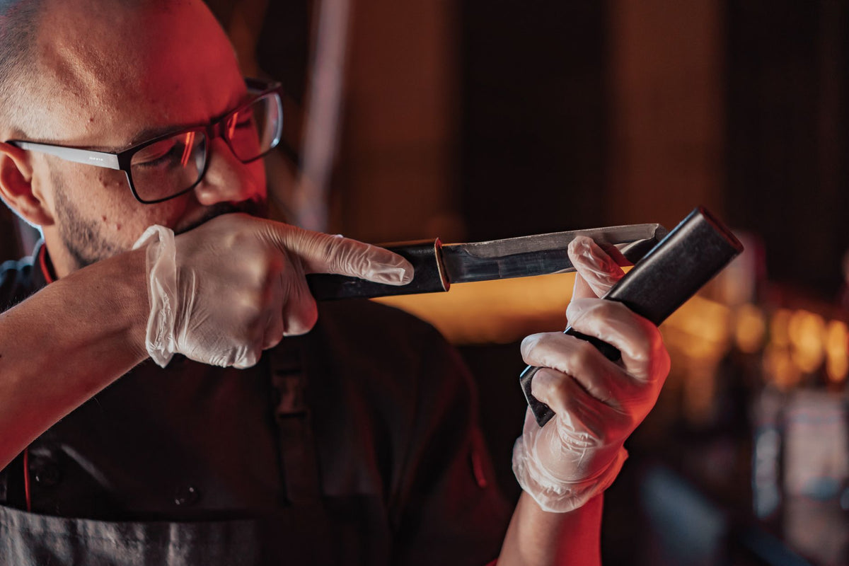A chef sharpening a knife with precision in a warm-lit kitchen, wearing latex gloves and glasses.