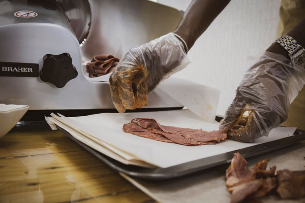 Hands in gloves slicing beef on a meat slicer, showcasing kitchen work in Angola.