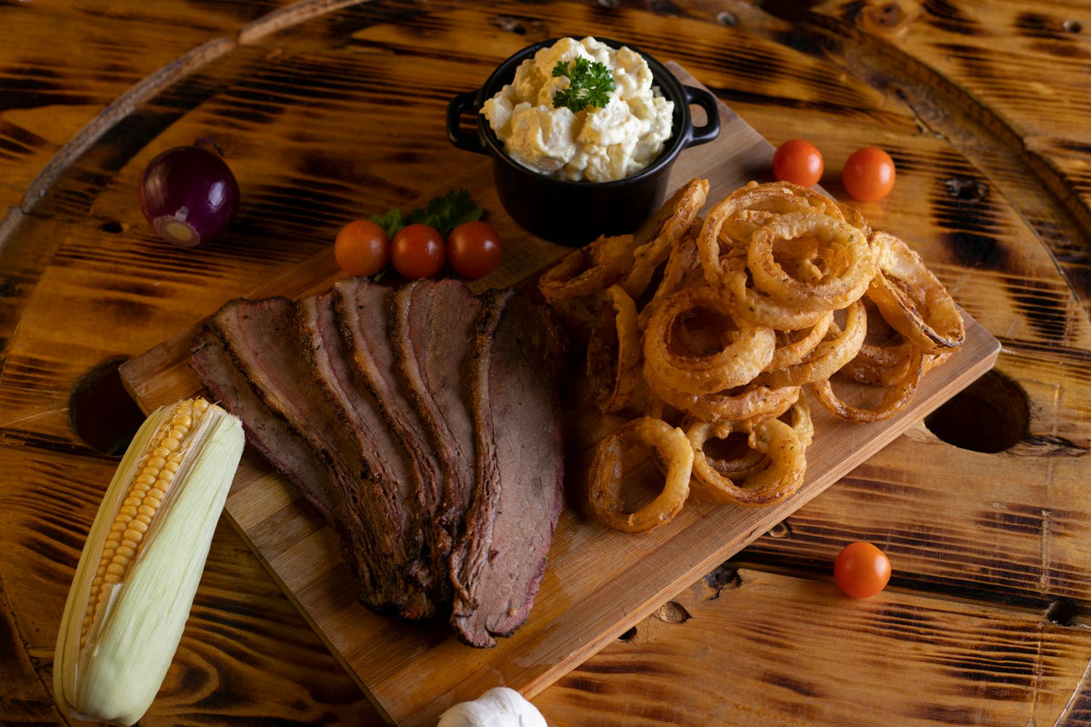 Delicious BBQ platter featuring tender steak, crispy onion rings, and fresh side dishes on a wooden board.