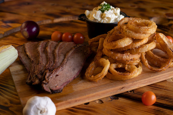Delicious slices of beef steak served with crispy onion rings, tomatoes, and creamy potato salad on a wooden platter.